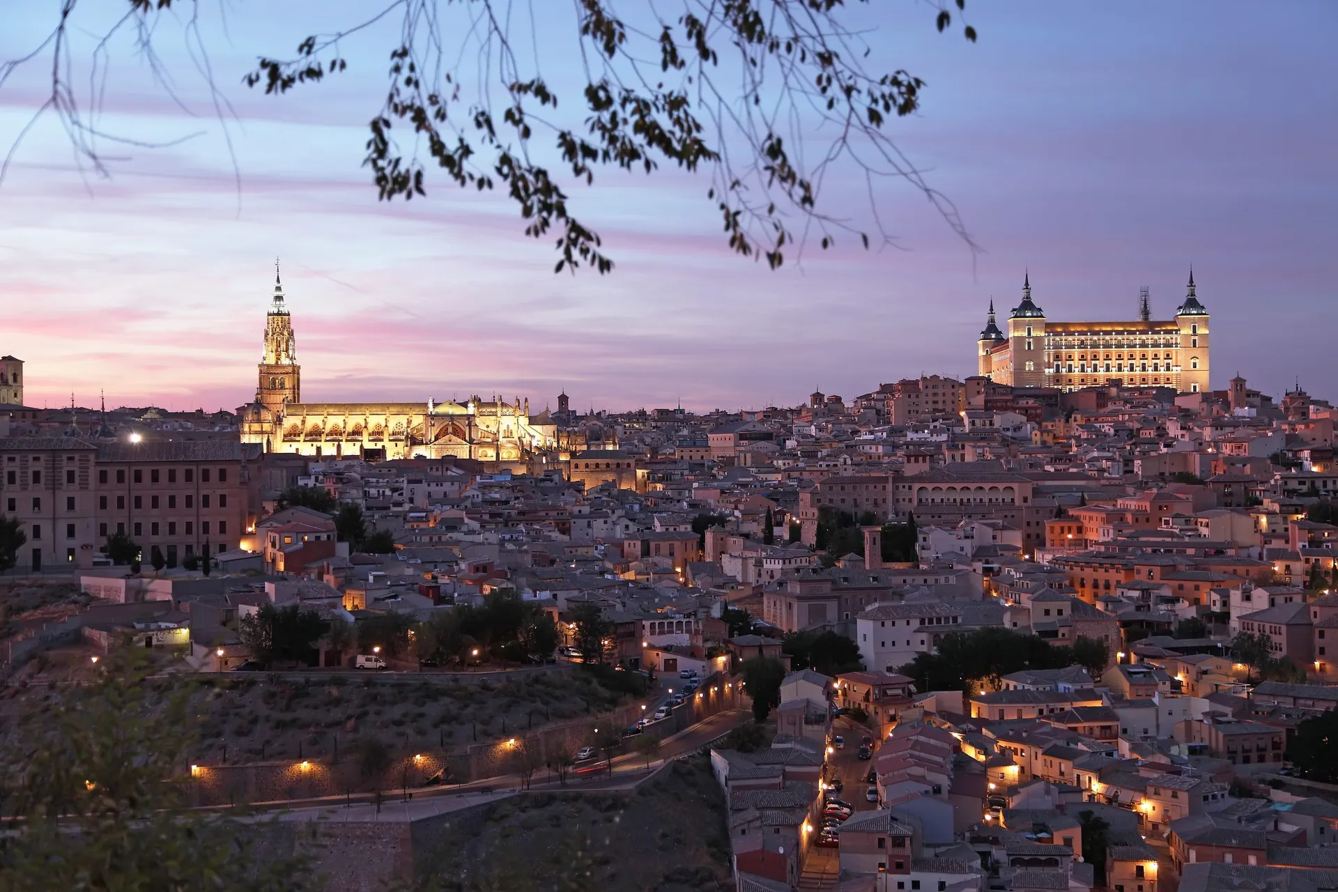 Toledo at dusk, with the cathedral tower and the Alcázar lit above the old town